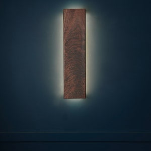 May include: A dark wood wall sconce with a warm white light emanating from behind it.
