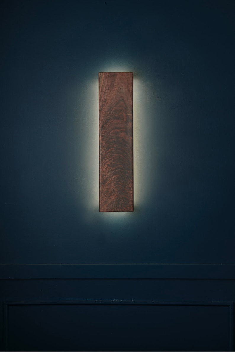 May include: A dark wood wall sconce with a warm white light emanating from behind it.