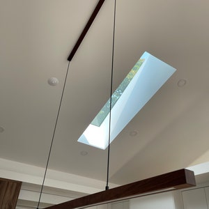 Peut inclure: Un luminaire suspendu moderne en bois de noyer avec un cordon noir suspendu à un plafond blanc. Le luminaire est suspendu à une poutre en bois.