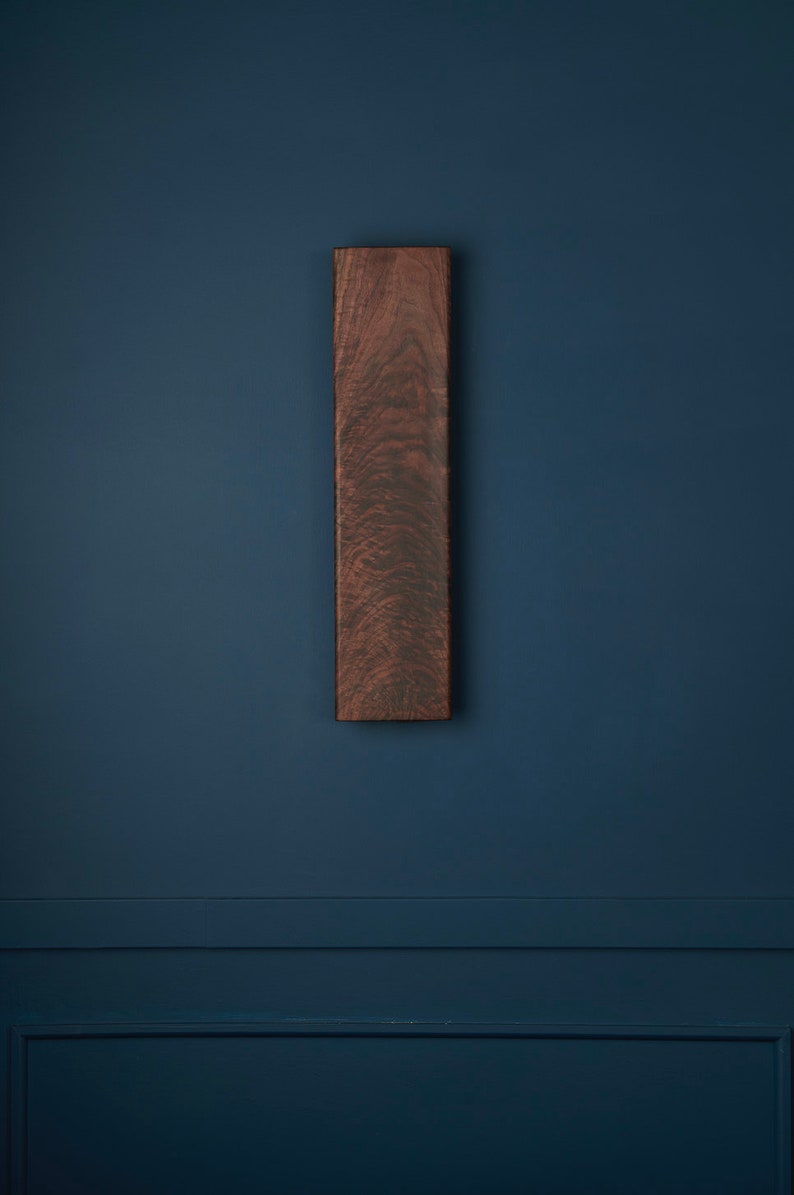 May include: A dark brown wooden rectangular sign with a wood grain pattern, mounted on a dark blue wall.