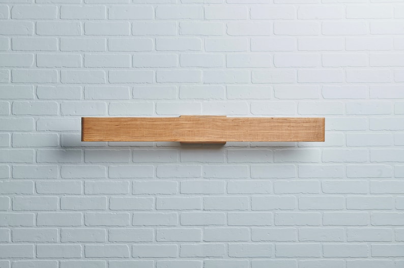 May include: A wooden light fixture mounted on a white brick wall. The fixture is a long, rectangular piece of wood with a slightly rounded edge.