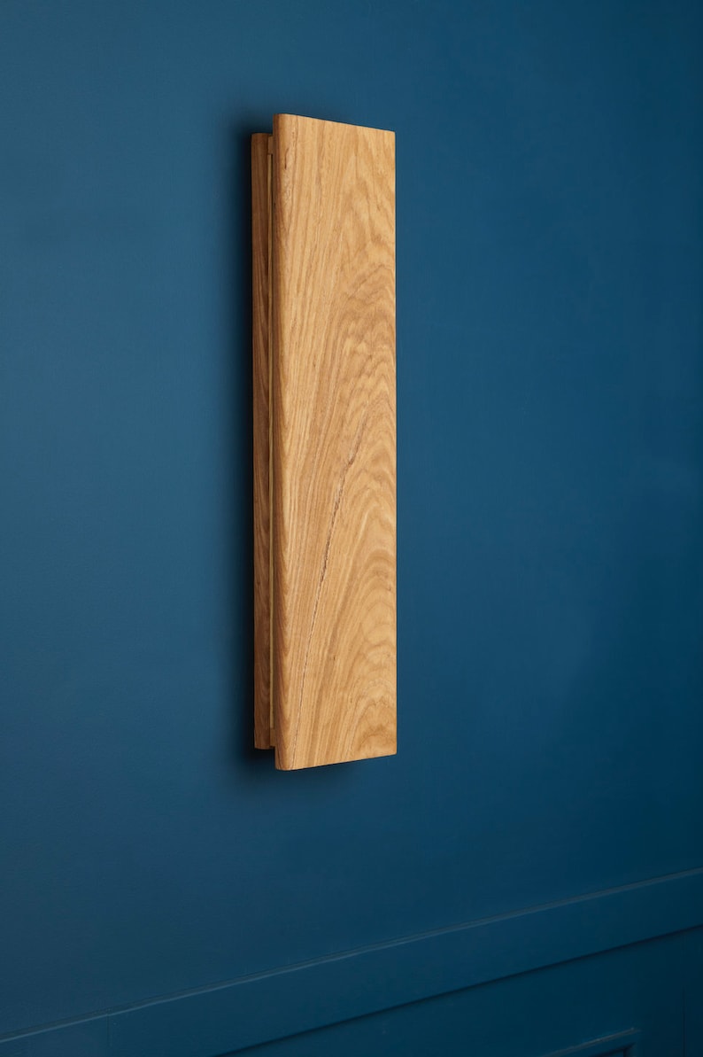 May include: A wooden wall sconce with a natural wood finish. The sconce is mounted on a blue wall.