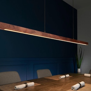 May include: A long, linear pendant light fixture crafted from dark brown wood with a smooth finish. The fixture is suspended by thin wires and features an integrated LED light strip running along the bottom edge, emitting a warm, downward glow.