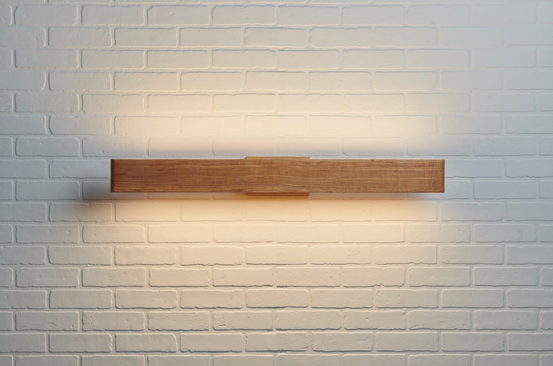 May include: A wooden wall sconce with a warm white light illuminating the white brick wall behind it.