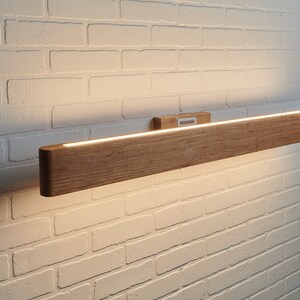May include: A wooden wall sconce with a built-in LED light strip. The sconce is mounted on a white brick wall.