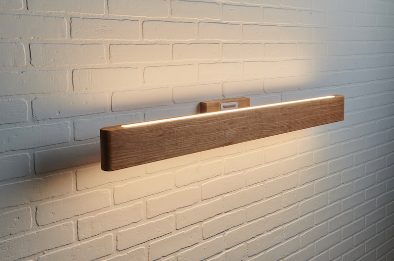 May include: A wooden wall sconce with a built-in LED light strip. The sconce is mounted on a white brick wall.