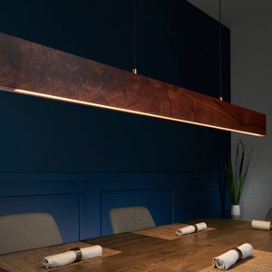 May include: A dark wood rectangular pendant light fixture hangs over a dining table with two chairs. The light fixture has a warm white light that illuminates the table and chairs.