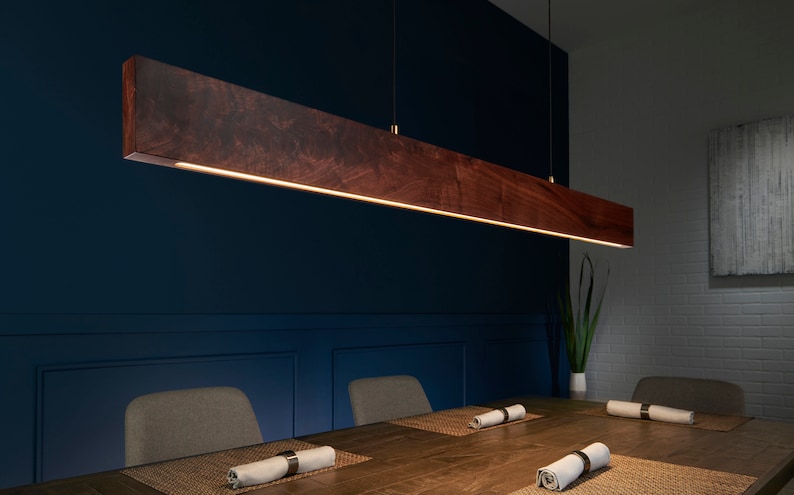 May include: A dark wood rectangular pendant light fixture hangs over a dining table with two chairs. The light fixture has a warm white light that illuminates the table and chairs.