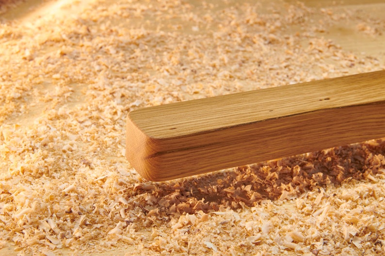 May include: A close-up of a wooden plank resting on a bed of wood shavings. The plank is light brown and has a smooth, polished surface.