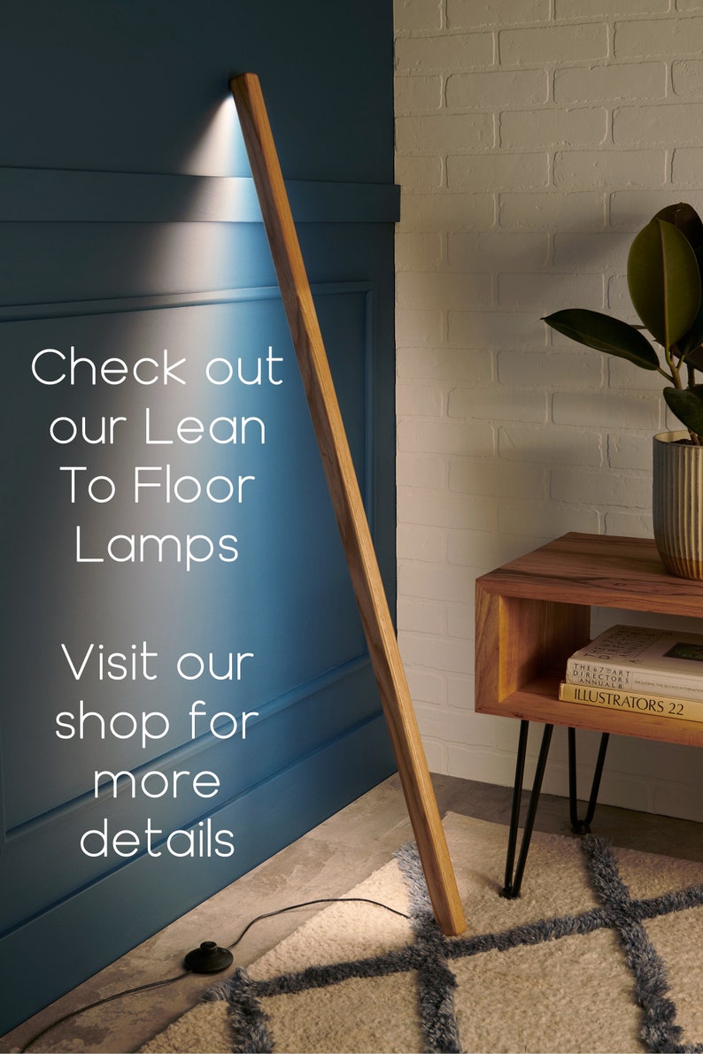May include: A wooden floor lamp with a long, slender design. The lamp is leaning against a wall and casting a warm light. The lamp is on a rug with a geometric pattern. The text "Check out our Lean To Floor Lamps Visit our shop for more details" is visible in the image.