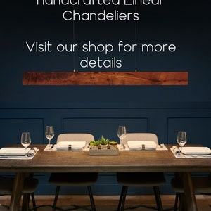 May include: A dark wood dining table with six chairs, set with place settings and a centerpiece of potted succulents. A wooden linear chandelier hangs above the table against a dark blue wall. The text "Check out our handcrafted Linear Chandeliers Visit our shop for more details" is displayed above the chandelier.