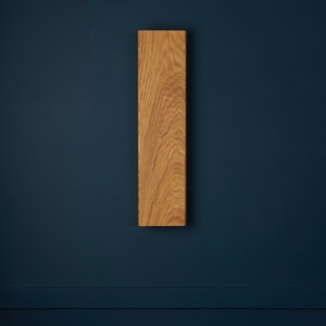May include: A vertical wooden wall shelf with a natural wood finish. The shelf is mounted on a dark blue wall.