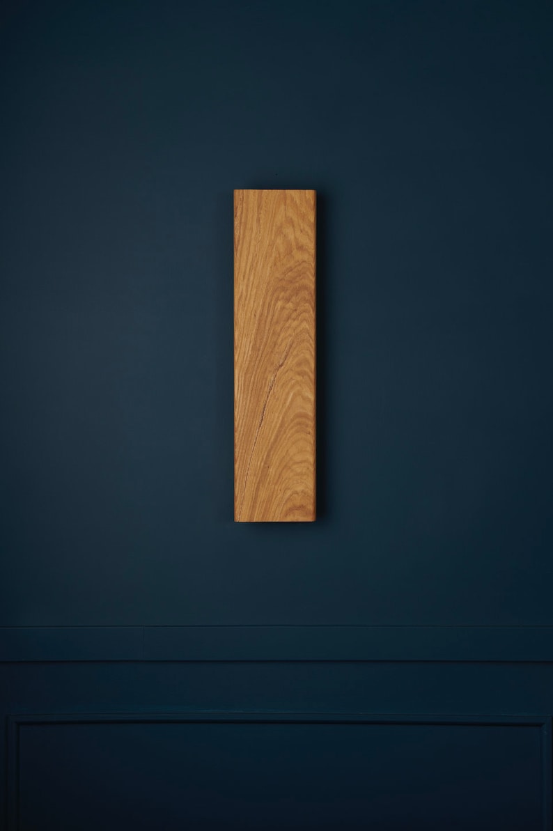 May include: A vertical wooden wall shelf with a natural wood finish. The shelf is mounted on a dark blue wall.