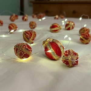 Puede incluir: Una cadena de luces blancas con adornos decorativos rojos y dorados sobre una colcha blanca.