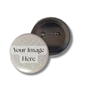 Op de afbeelding: Een ronde button met een zilveren glitterafwerking. De voorkant van de button bevat de zwarte tekst Your Image Here gedrukt op een witte rechthoekige achtergrond. Een tweede button is erachter geplaatst, met de metalen achterkant en speld.