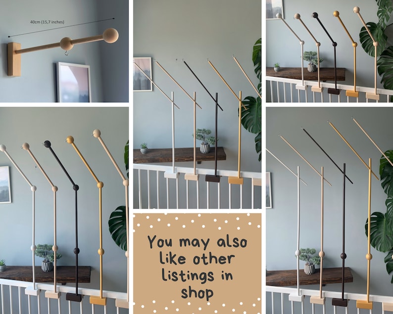 May include: A set of wooden baby mobile arms in various colors, including black, white, gold, and natural wood. The arms are designed to be mounted on a railing or wall and feature a swiveling arm with a wooden ball at the end. The arms are 40cm (15.7 inches) long.