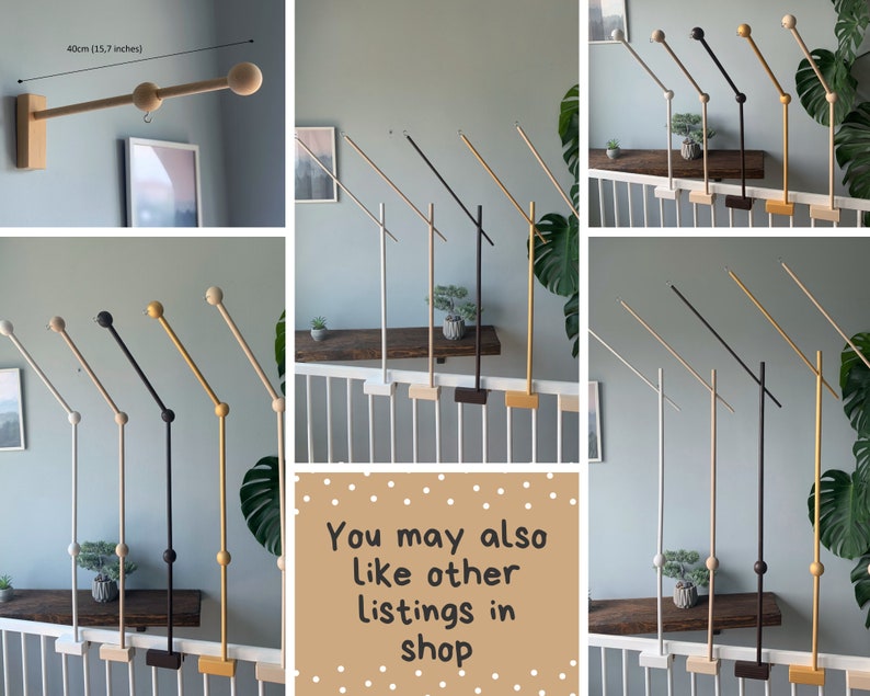 May include: A set of wooden baby mobile arms in various colors, including black, white, gold, and natural wood. The arms are designed to be mounted on a railing or wall and feature a swiveling arm with a wooden ball at the end. The arms are 40cm (15.7 inches) long.
