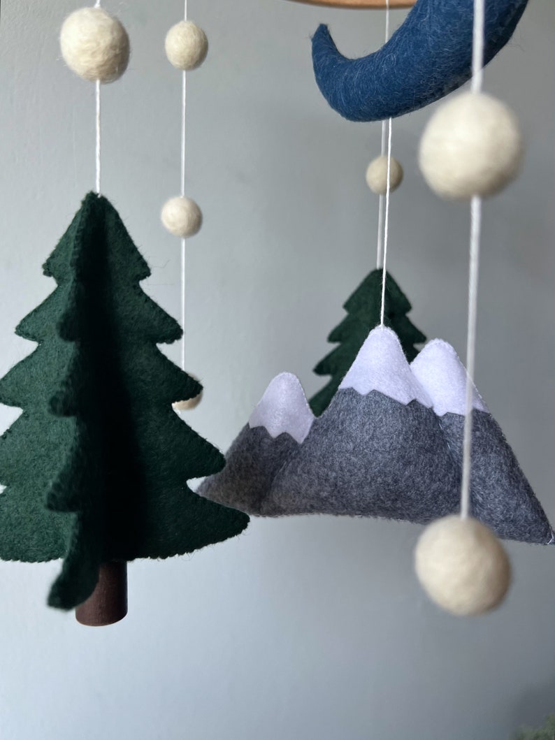 May include: A felt baby mobile with a green tree, gray mountains with white snow peaks, a blue crescent moon, and white felt balls.