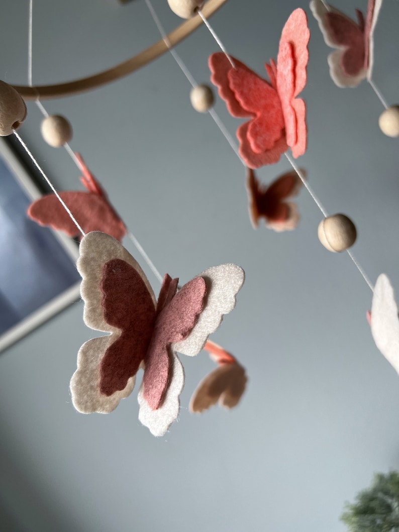 May include: A wooden mobile with pink and white felt butterflies and wooden beads hanging from it.