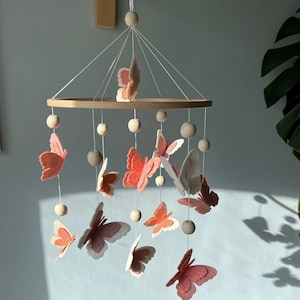 May include: A wooden baby mobile with a circular wooden frame and pink and white felt butterflies hanging from it. The mobile is decorated with wooden beads.