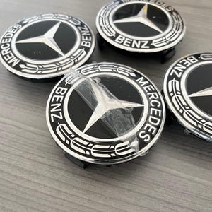 May include: Four black and silver Mercedes-Benz car hubcaps with the words "Mercedes-Benz" and "Benz" printed on them.