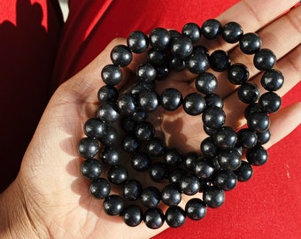 May include: A close-up of a black beaded bracelet. The bracelet is made of round, smooth beads and is stacked on top of itself.