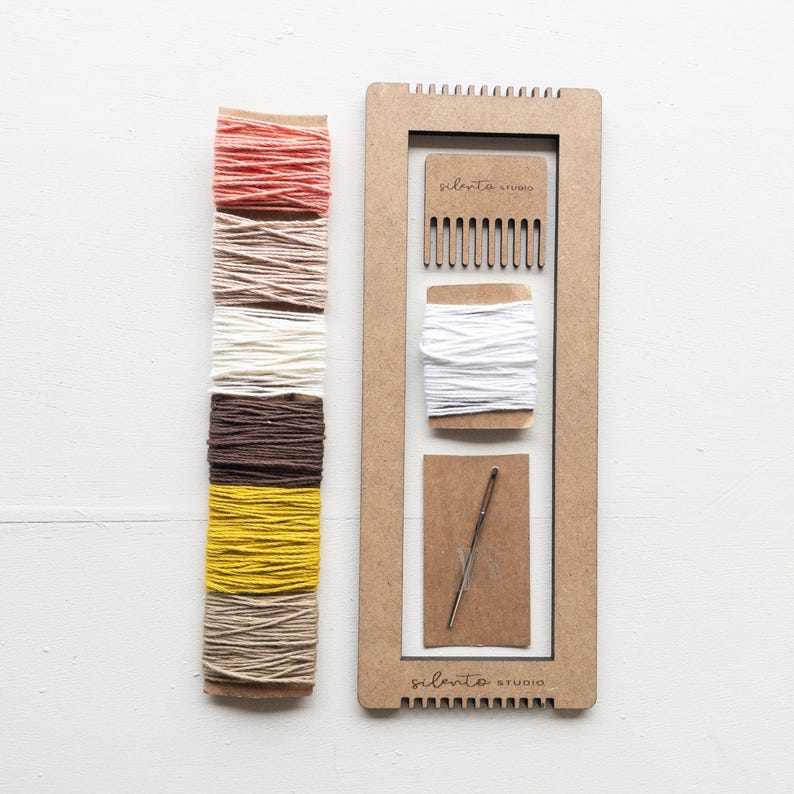 Op de afbeelding: Een knutselset met een houten weefgetouw, een kam, een naald en spoelen met kleurrijk garen. De garenkleuren zijn koraal, beige, cr&egrave;me, bruin, geel en beige. De tekst "silento studio" staat op het weefgetouw.