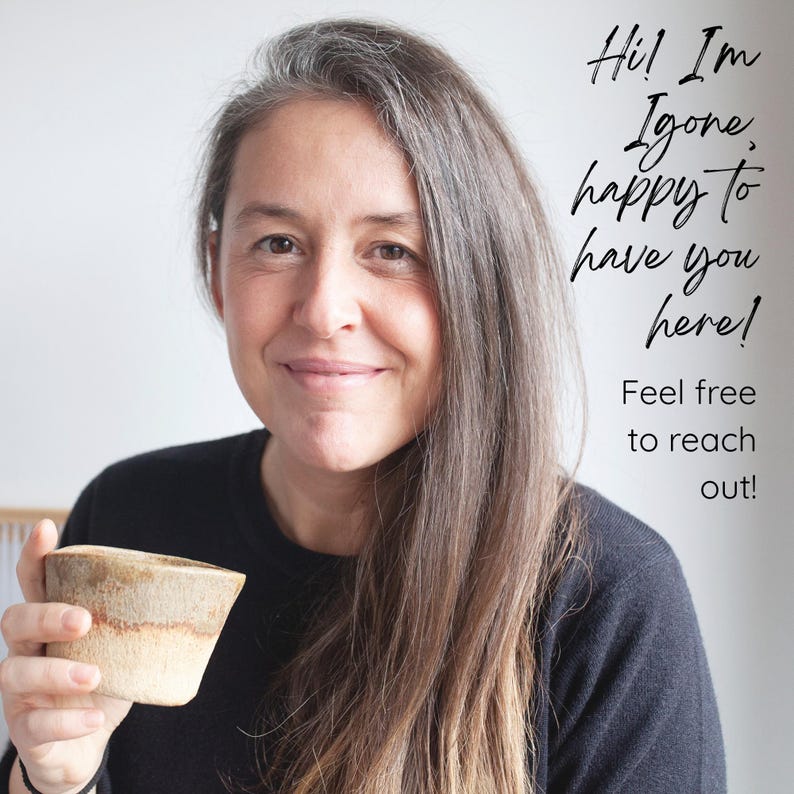 Op de afbeelding: Een vrouw met lang grijs haar glimlacht, terwijl ze een kleine, beige keramische kom vasthoudt. De afbeelding bevat de tekst "Hi! I'm Igone, happy to have you here! Feel free to reach out!"