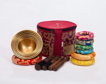 May include: A set of seven singing bowls with a red cushion, four wooden strikers, and a stack of colorful cushions in a red carrying case with the text "Singing Bowls".