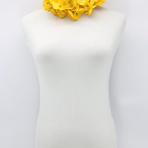 May include: A vibrant yellow floral necklace displayed on a white mannequin. The necklace features numerous bright yellow flower petals, creating a full, eye-catching design. The necklace is a statement piece, perfect for adding a pop of color.