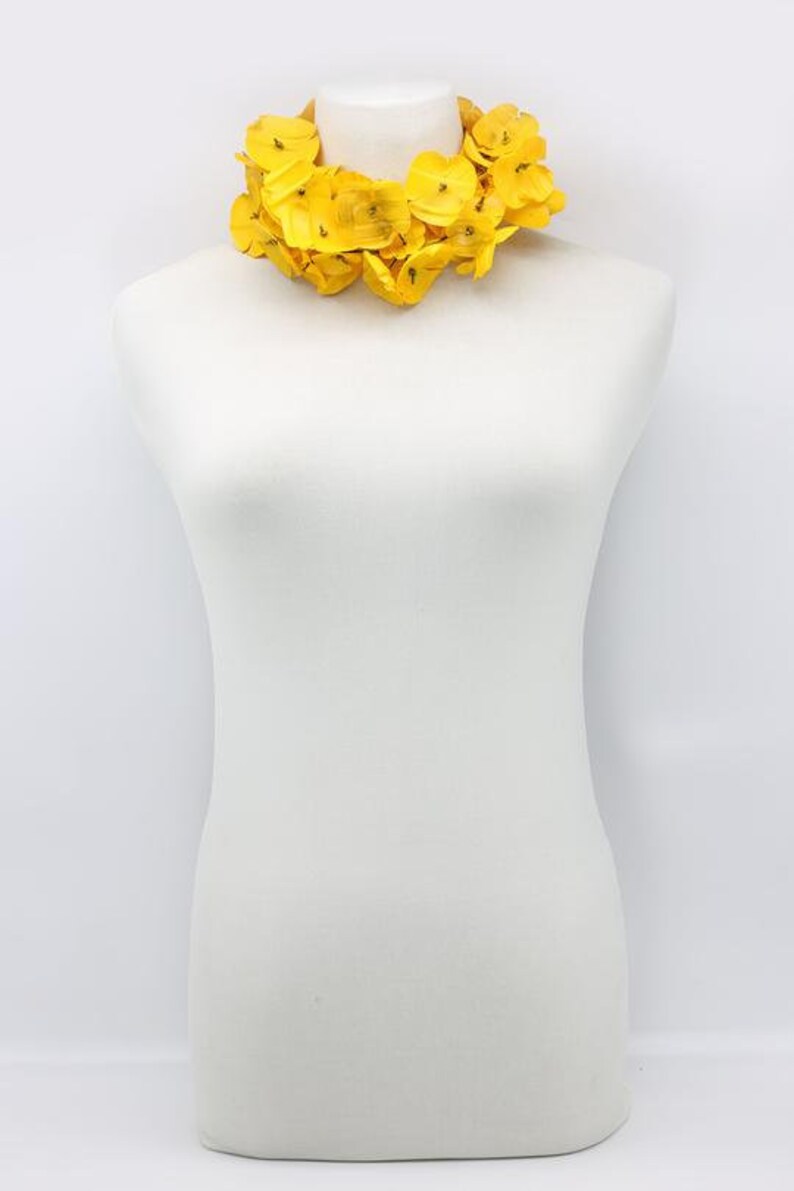 May include: A vibrant yellow floral necklace displayed on a white mannequin. The necklace features numerous bright yellow flower petals, creating a full, eye-catching design. The necklace is a statement piece, perfect for adding a pop of color.
