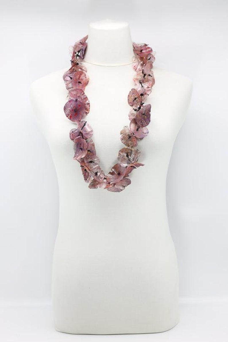 May include: A necklace made of translucent, petal-shaped beads in shades of pink and purple. The beads are strung together to form a statement piece, displayed on a white mannequin. The necklace has a delicate, floral appearance.