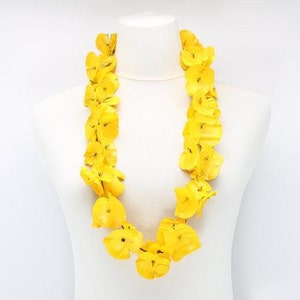 May include: A vibrant yellow lei necklace displayed on a white mannequin. The lei is composed of numerous bright yellow flower petals, creating a full and eye-catching garland. The necklace is a traditional Hawaiian accessory.