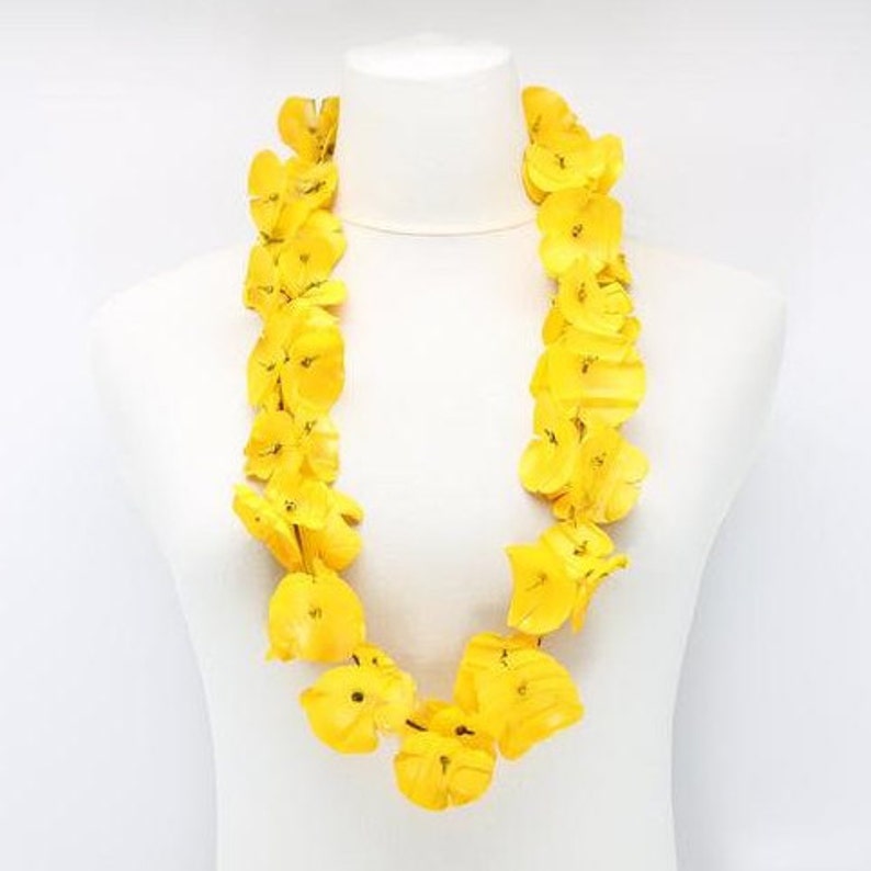 May include: A vibrant yellow lei necklace displayed on a white mannequin. The lei is composed of numerous bright yellow flower petals, creating a full and eye-catching garland. The necklace is a traditional Hawaiian accessory.