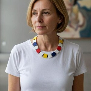 May include: A necklace featuring a series of square-shaped beads in primary colors including red, yellow, blue, and white, arranged in a repeating pattern around the neck, worn with a plain white short-sleeved t-shirt.