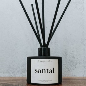 Puede incluir: Botella de vidrio negro mate con cañas negras y una etiqueta blanca que dice "The monastery candle co. Santal Difusor de cañas de aceite natural 8 oz / 237 ml"