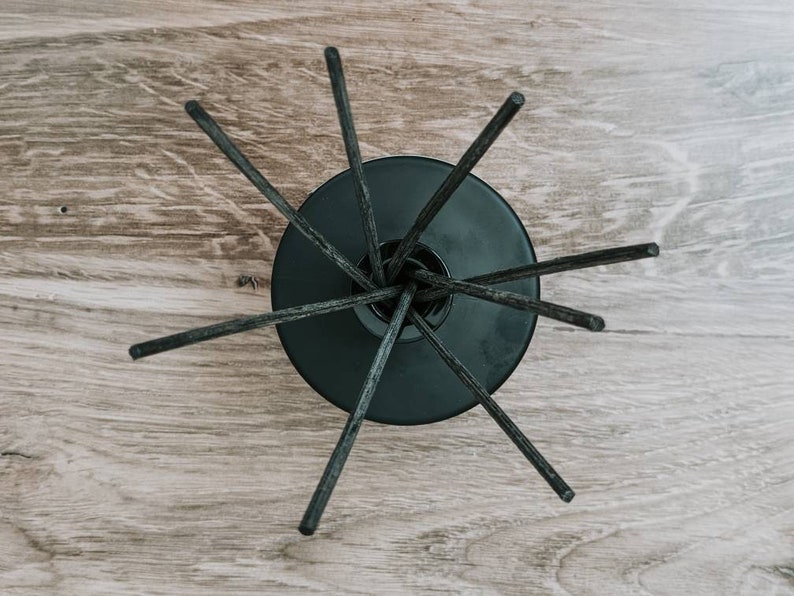 May include: Black diffuser sticks radiating out from a black ceramic base on a wood surface.
