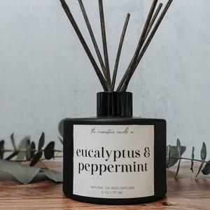May include: Black glass diffuser bottle with a white label that reads "the moonstone candle co eucalyptus & peppermint NATURAL OIL REED DIFFUSER 6 OZ/177 ML". The bottle is filled with a clear liquid and has black reeds sticking out of the top.