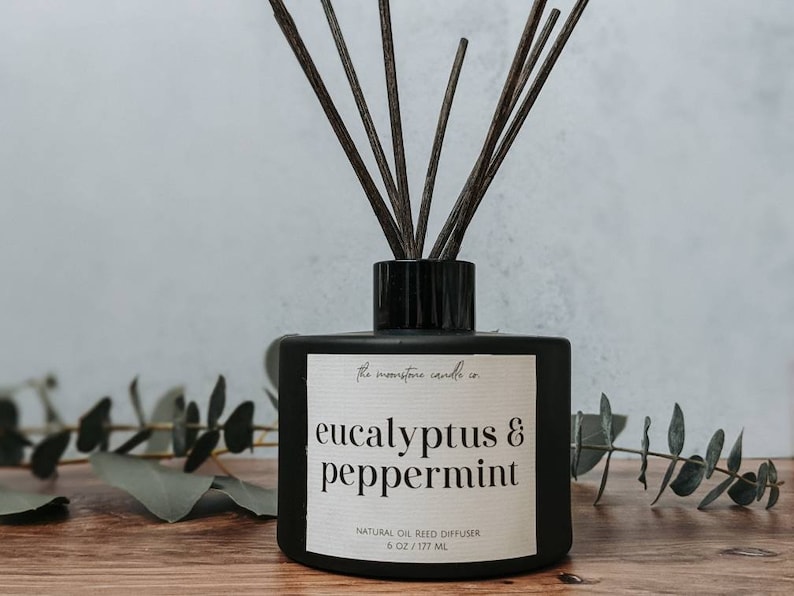 May include: Black glass diffuser bottle with a white label that reads "the moonstone candle co eucalyptus & peppermint NATURAL OIL REED DIFFUSER 6 OZ/177 ML". The bottle is filled with a clear liquid and has black reeds sticking out of the top.