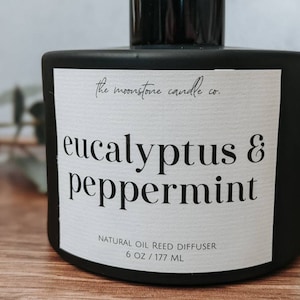 May include: Black glass bottle with a white label that reads "the moonstone candle co. eucalyptus & peppermint NATURAL OIL REED DIFFUSER 6 OZ/177 ML"