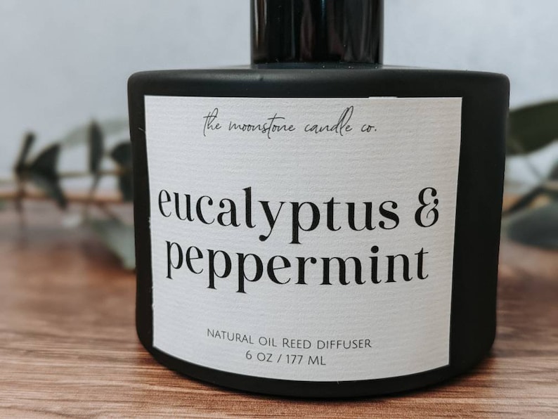 May include: Black glass bottle with a white label that reads "the moonstone candle co. eucalyptus & peppermint NATURAL OIL REED DIFFUSER 6 OZ/177 ML"