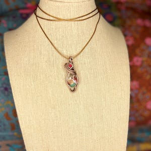 May include: A gold chain necklace with a pendant featuring a multi-colored stone wrapped in wire and a red gemstone accent.