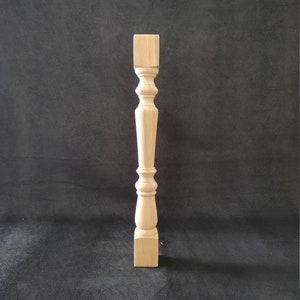 May include: A wooden table leg with a square base and a turned design. The leg is made of unfinished wood and has a natural color.