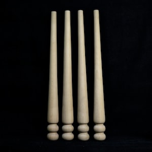 May include: Four wooden table legs with a rounded top and a decorative design. The legs are light brown and are arranged in a row against a black background.