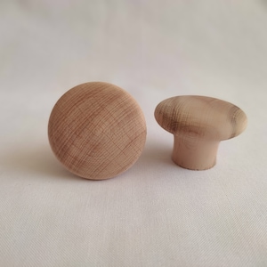 May include: Two wooden knobs, one round and one with a stem. Both are a light brown color with a wood grain pattern.