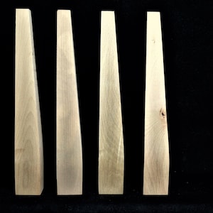 May include: Four wooden tapered dowels, each with a slightly different grain pattern. The dowels are light brown in color and have a smooth, polished finish.