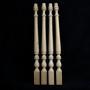 May include: Four unfinished wooden balusters with decorative turned details. Each baluster has a square base, a series of rounded and tapered sections, and a top with a small, rounded finial. The wood has a light, natural colour.