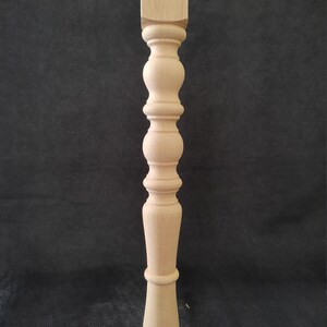 K&ouml;nnte beinhalten: Ein Tischbein aus Holz mit gedrehtem Design. Das Bein ist aus hellem Holz gefertigt und hat eine quadratische Oberseite und eine abgerundete Unterseite.