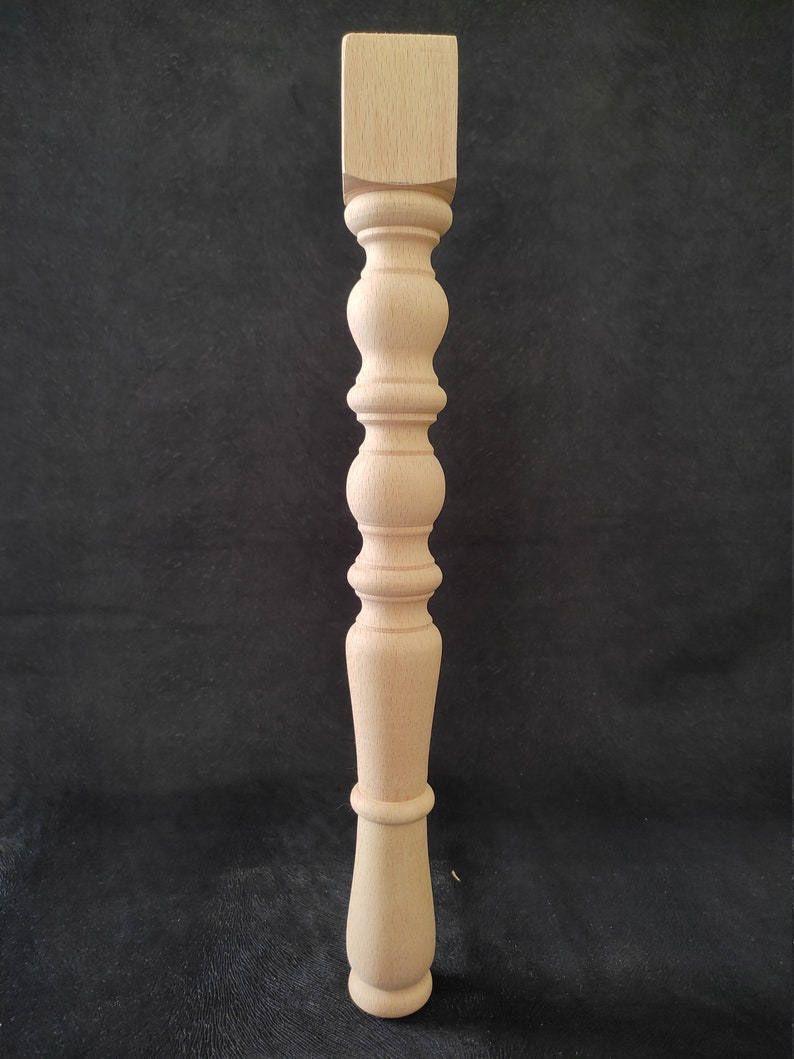 K&ouml;nnte beinhalten: Ein Tischbein aus Holz mit gedrehtem Design. Das Bein ist aus hellem Holz gefertigt und hat eine quadratische Oberseite und eine abgerundete Unterseite.