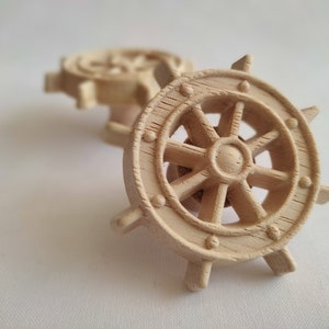 Könnte beinhalten: Zwei hölzerne Schiffsrad-Ornamente. Das größere Rad ist scharf gestellt und hat ein detailliertes Design mit acht Speichen. Das kleinere Rad ist im Hintergrund unscharf.